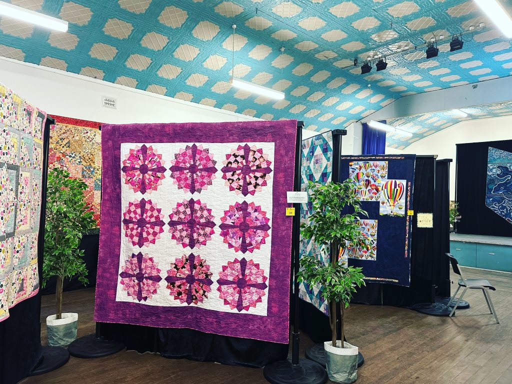 a series of brightly coloured quilts hanging on frames at an exhibition.