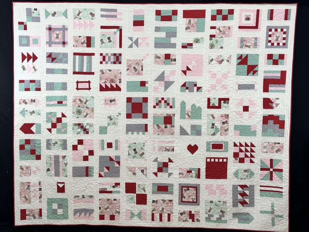 A white, red, pink, grey and green quilt.